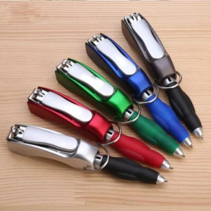 Five multifunction pen keychains in red, green, blue, grey and black laid out on a wooden desk, each showing its folding nail clipper and ballpoint tip