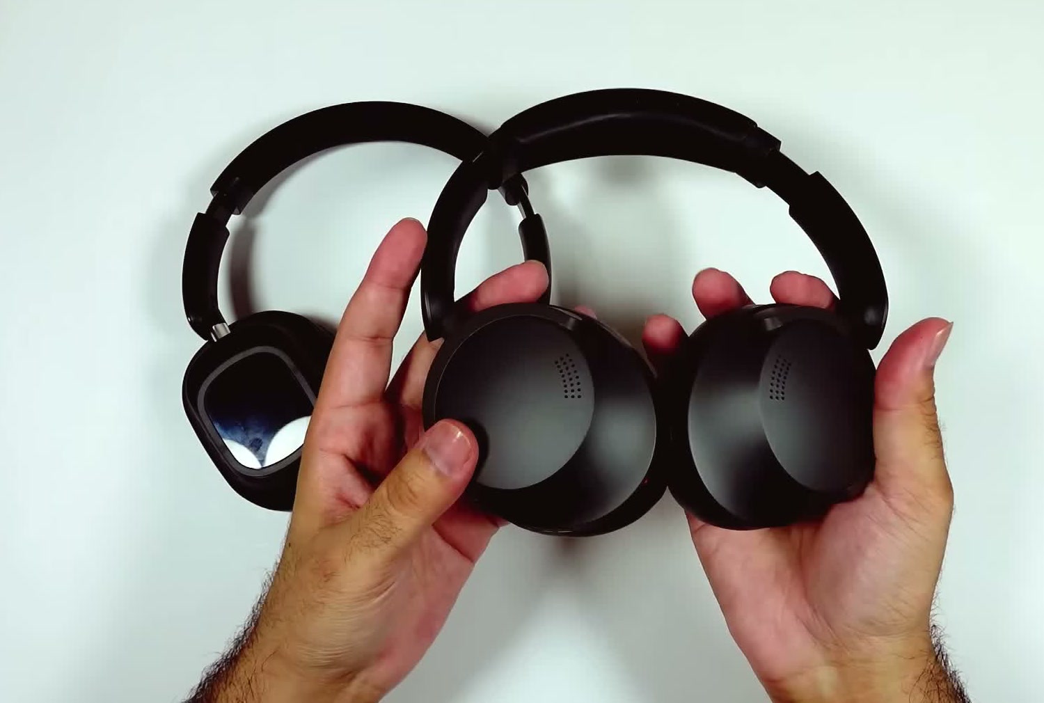 The actual pair of headphones held in both hands on a white desk, folded flat with both earcups facing forward