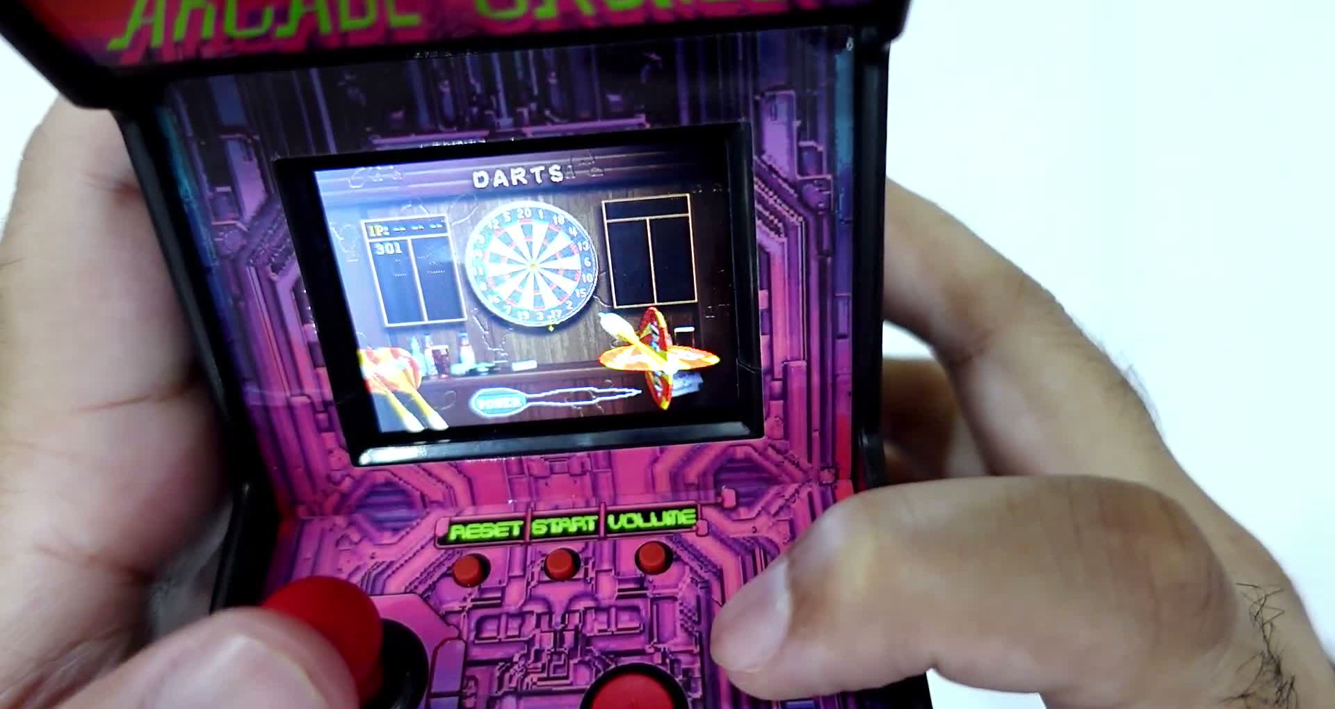 A darts game being played on the console's 2.5-inch colour screen, thumb on the joystick