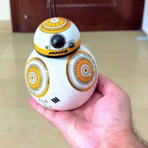 The actual RC robot droid ball held in one hand, showing its orange and white body markings and domed head