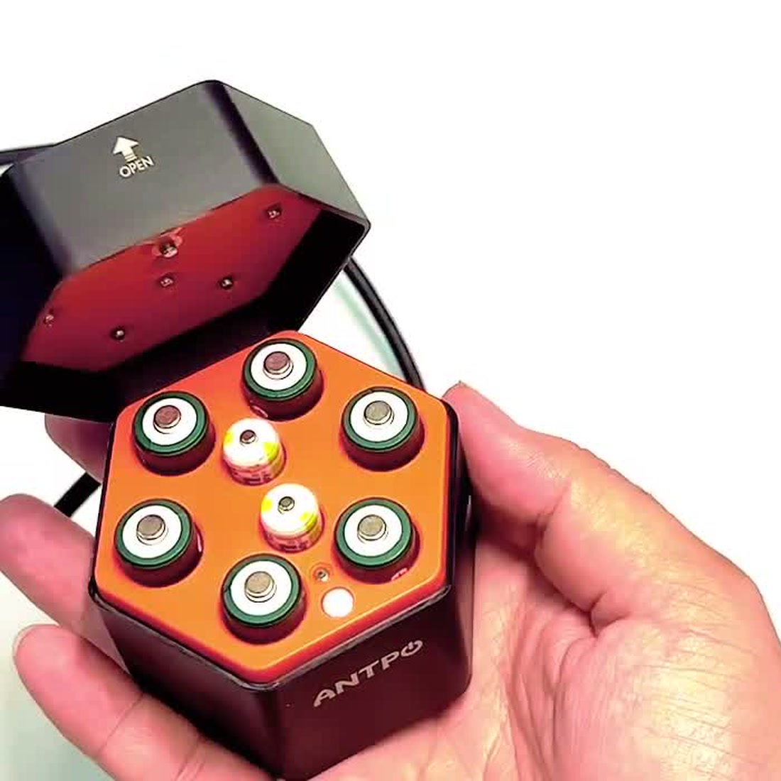 The actual charging case held open in hand with AA cells loaded and its charge indicator lights lit