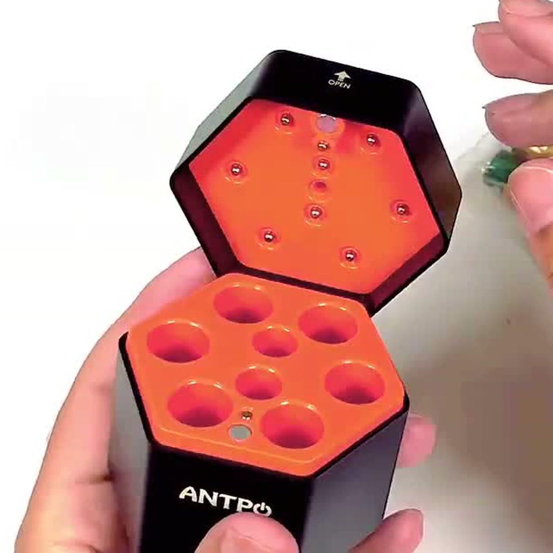 The charging case open and empty on the table, showing the orange cell tray and the ANTPO branding on the lid