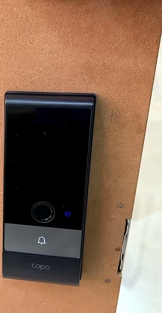 Tapo DL130 smart door lock installed on a door, seen at an angle showing its slim black front panel and Tapo branding