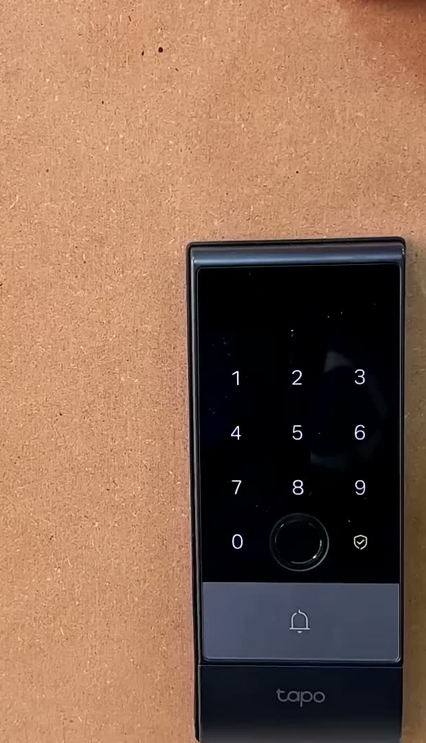 Lit backlit keypad of the Tapo DL130 smart door lock mounted on a door, with the fingerprint reader below the number pad