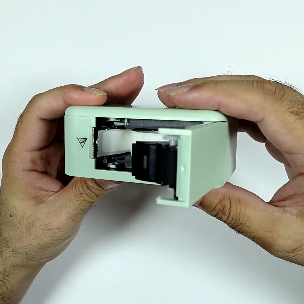 P15 label maker opened in two hands, showing the tape bay with the label roll seated and the thermal print head behind it