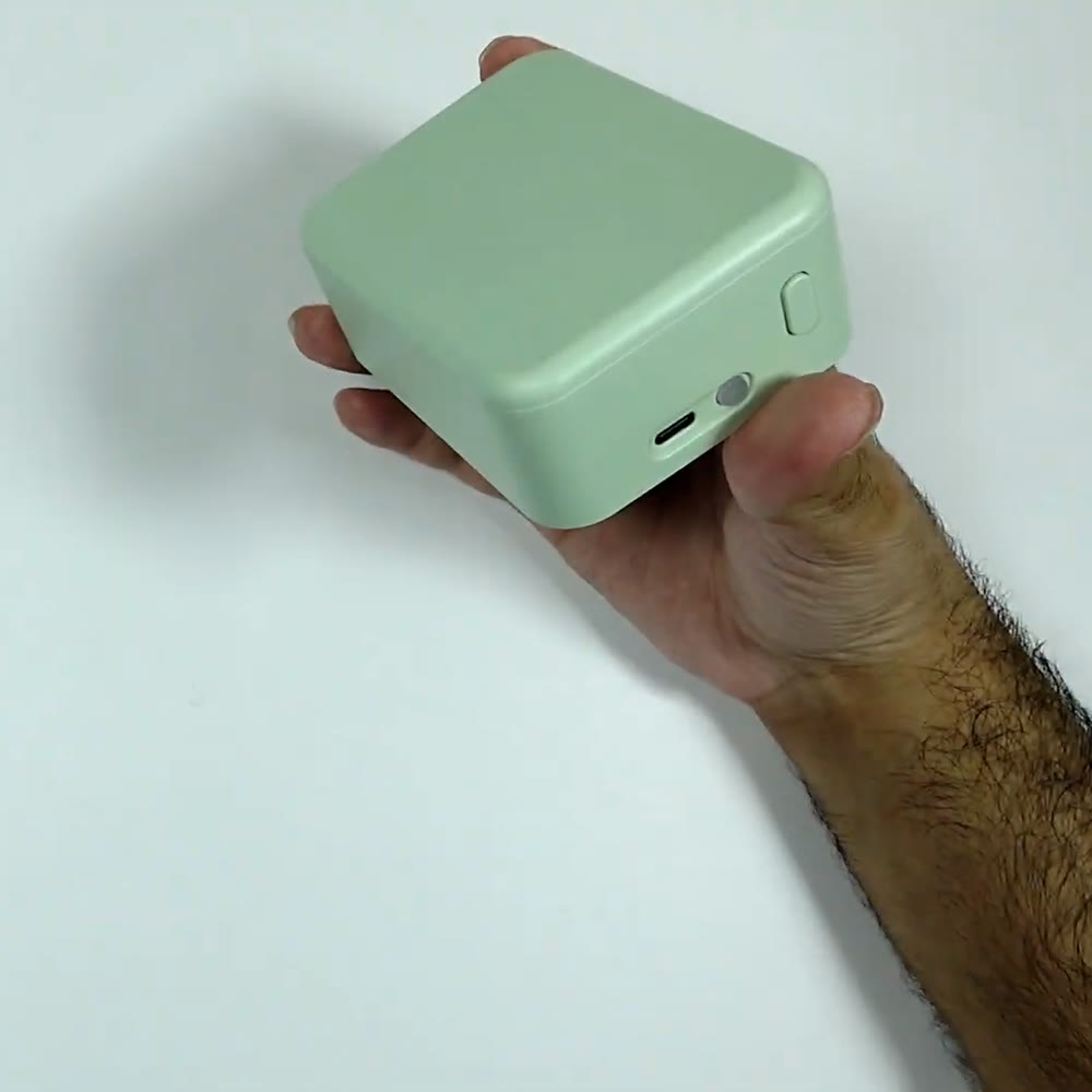 P15 Bluetooth label maker in mint green held in one hand over a white desk, showing the rounded body and the side power button
