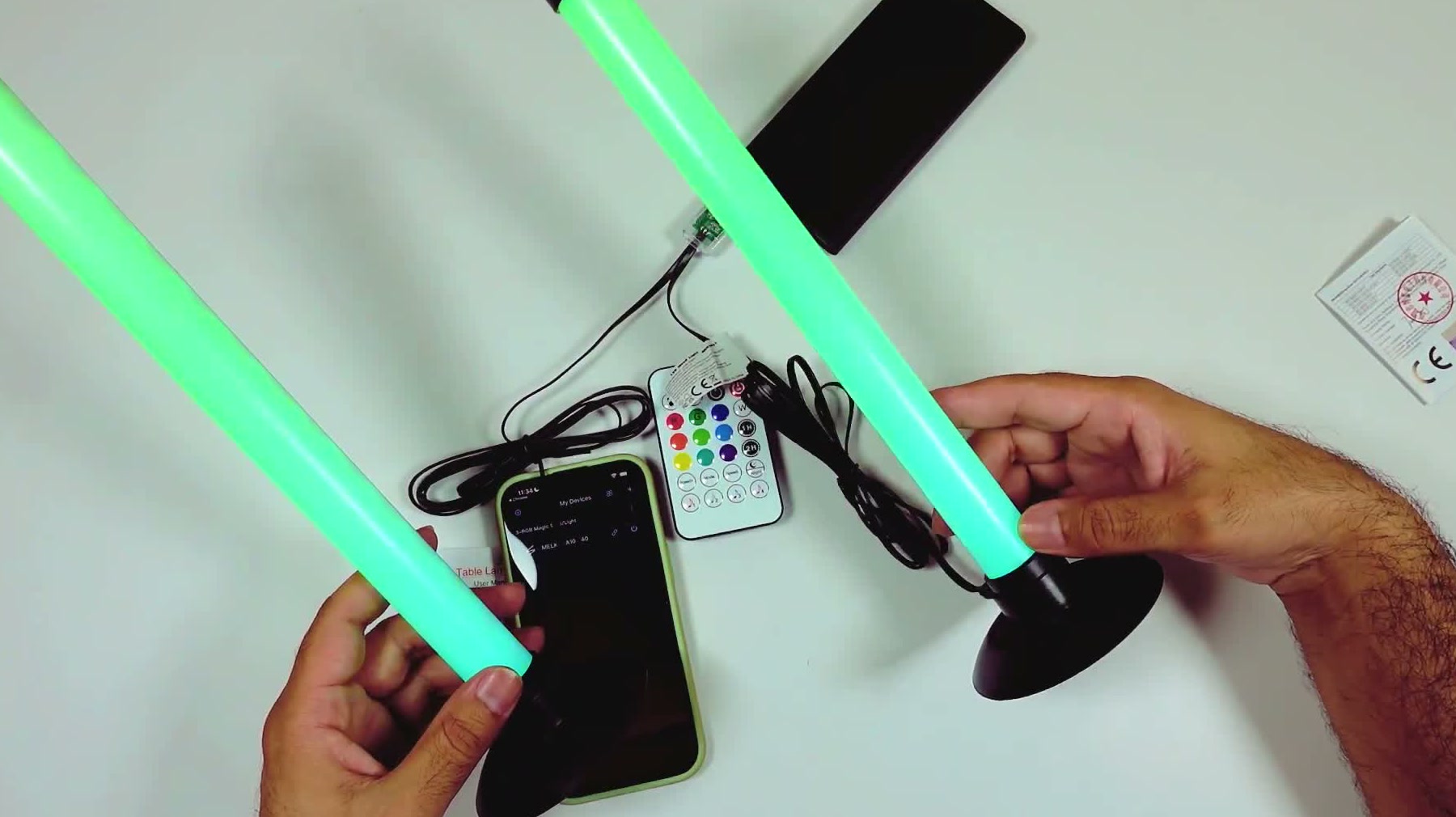 The actual pair of light bars lit bright green, held over a white desk beside the remote and USB cable