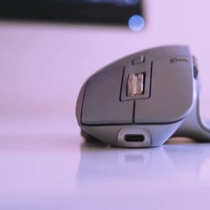 Logitech MX Master 3 in mid grey on a white desk, side profile showing the USB-C charging port
