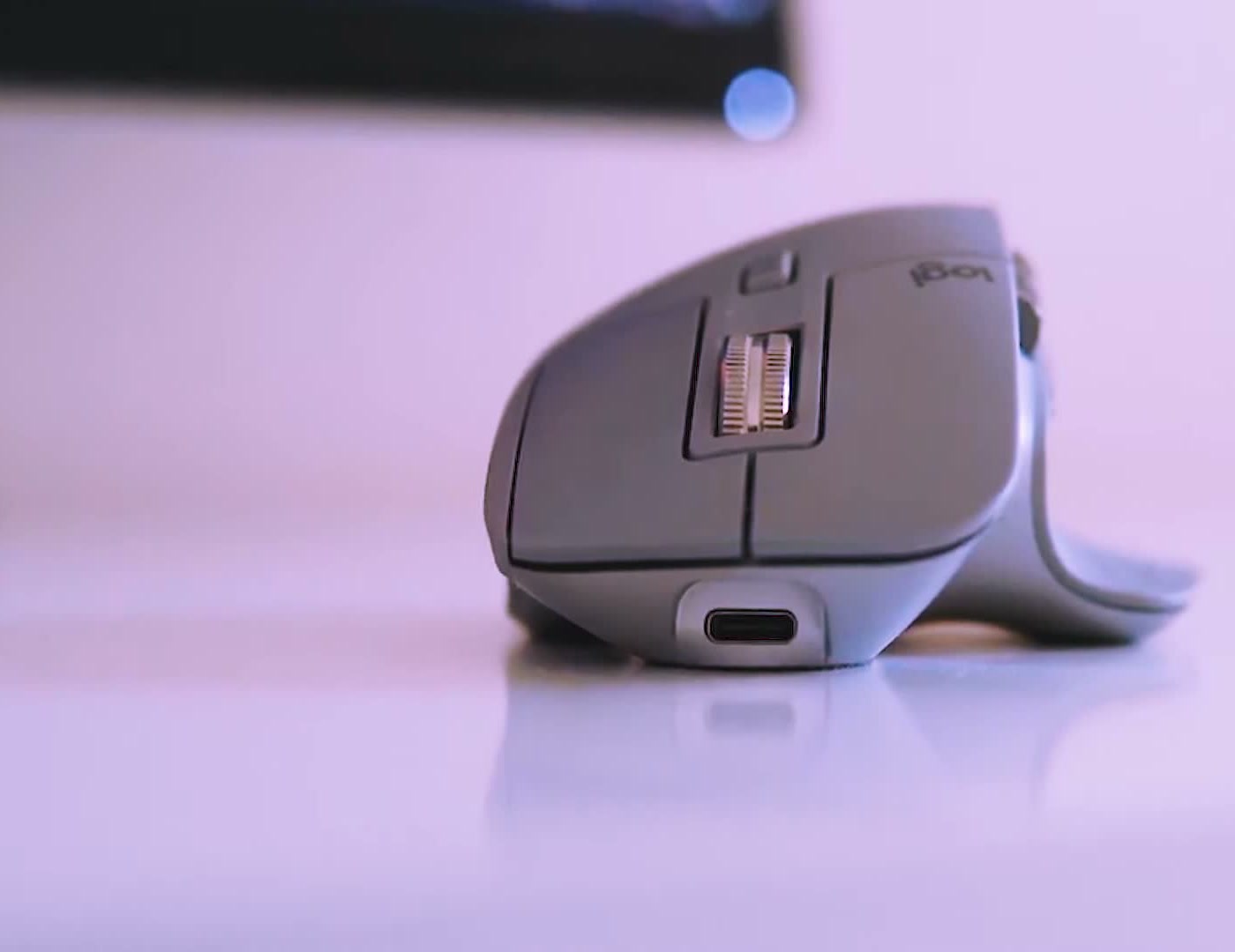 Logitech MX Master 3 in mid grey on a white desk, side profile showing the USB-C charging port
