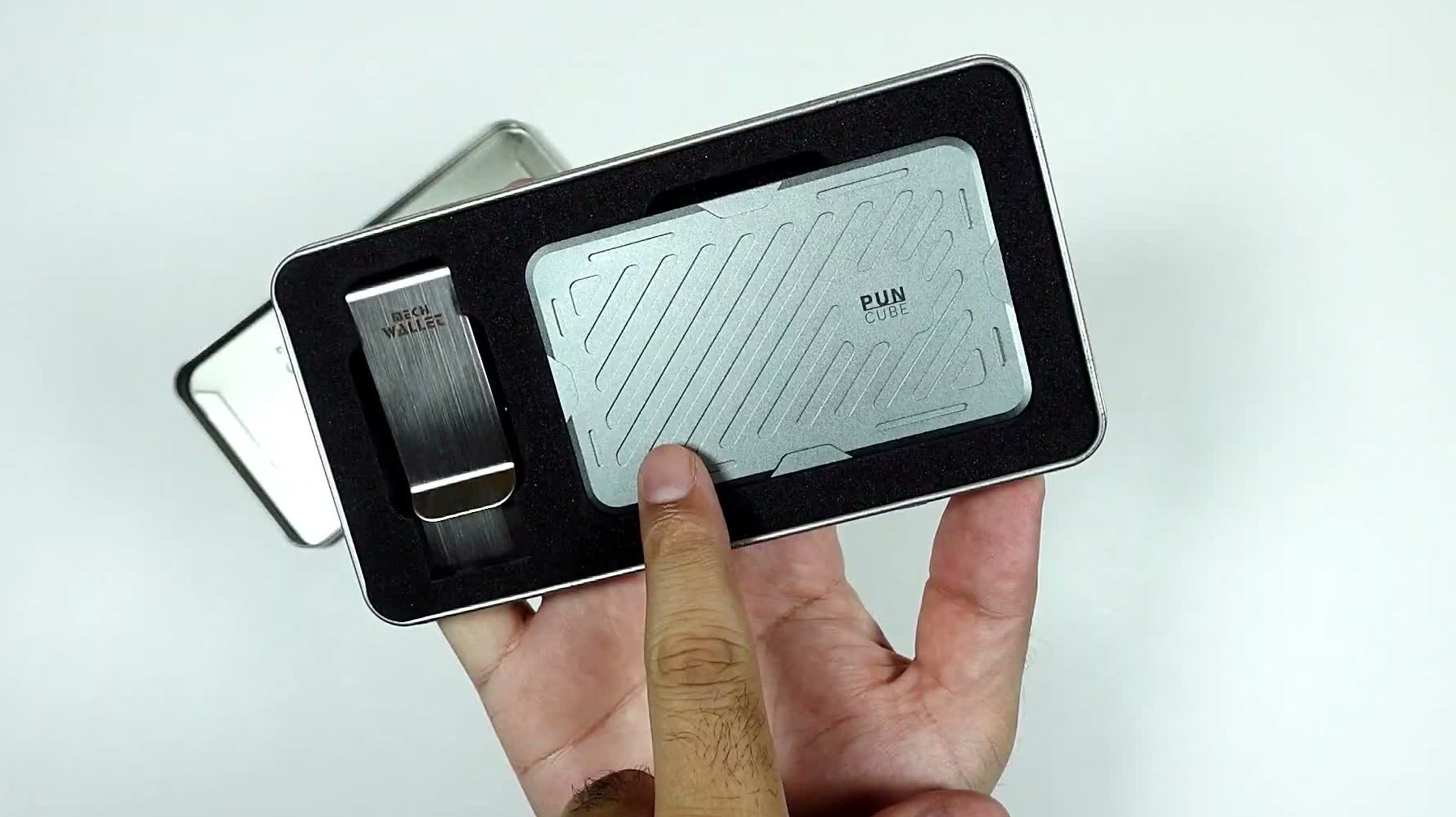 The wallet held in front of its open metal presentation tin, straight out of the box
