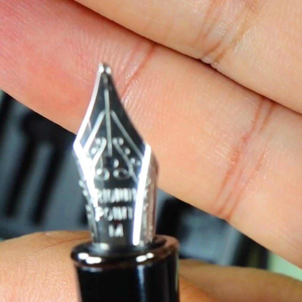 Close-up of the BAOKE stainless steel fountain pen nib held against a hand, showing the engraved iridium point marking