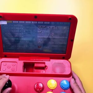 The red Powkiddy A13 arcade console open on a desk with the game menu on screen and both hands on the controls