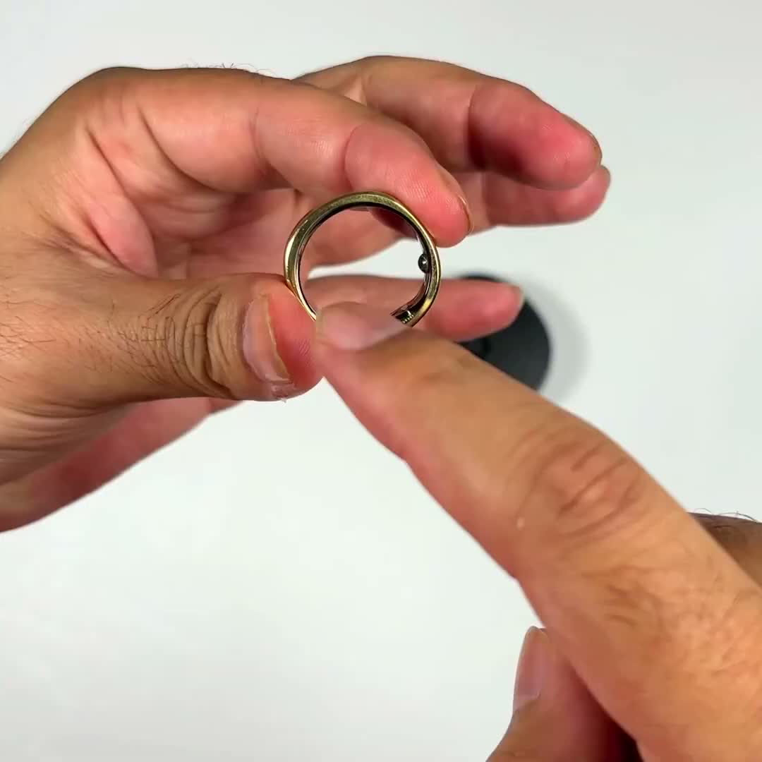 The actual gold RingConn Gen 2 smart ring held between the reviewer's fingers