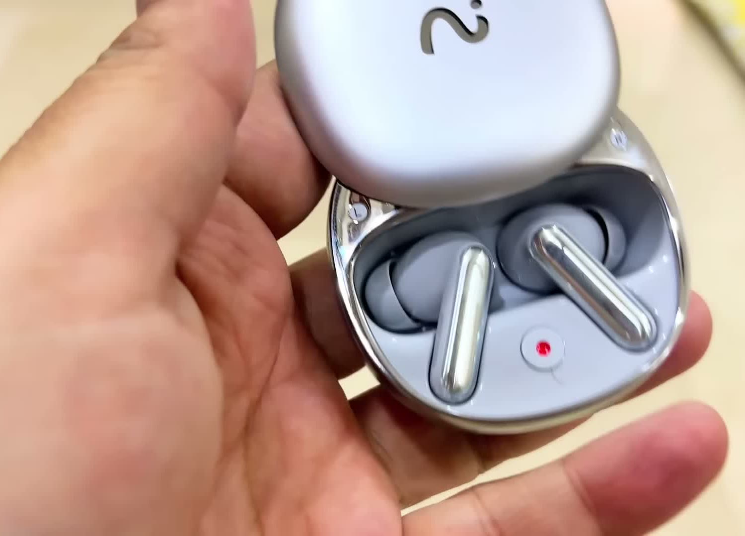 RecDot AI recorder earbuds held in hand, charging case open with both white earbuds seated inside