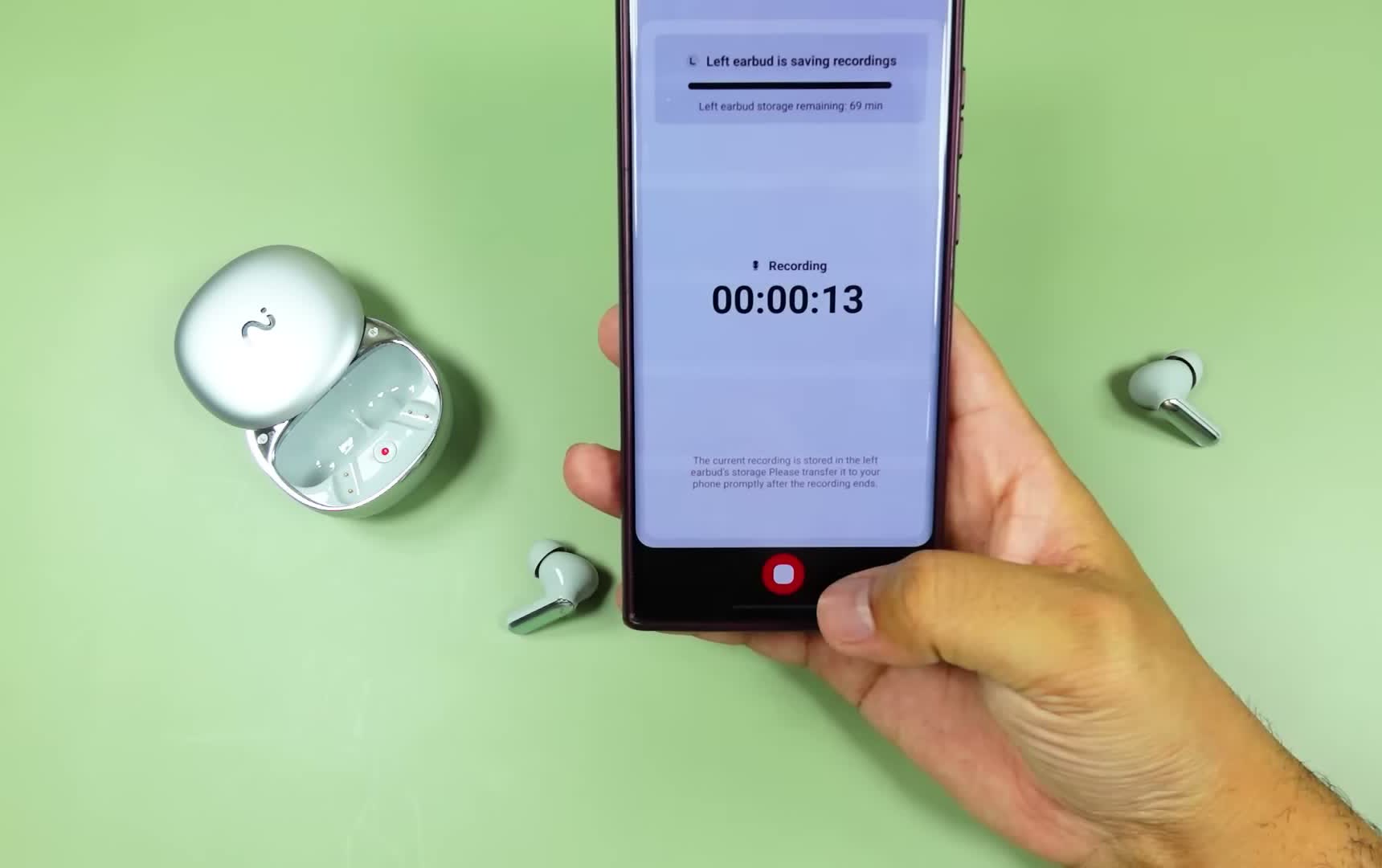 RecDot earbuds recording on a desk beside a phone showing a live recording timer, one earbud out of the case