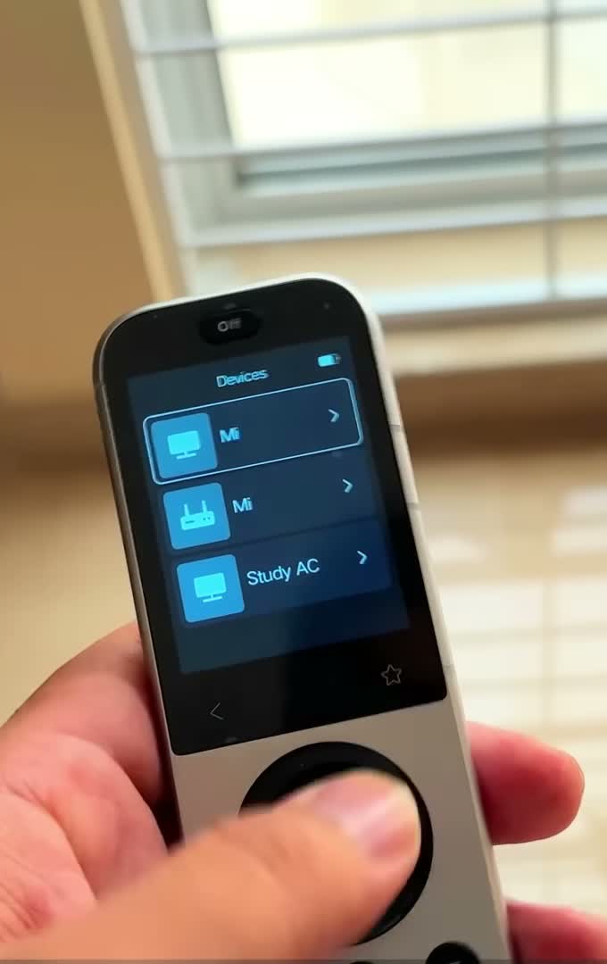 SofaBaton X2 remote held in hand, its colour touchscreen showing the paired device list