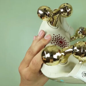 Cream SKG H7 Ultra E neck massager held in one hand, showing its six faceted gold kneading nodes and the red light-bead array on the body