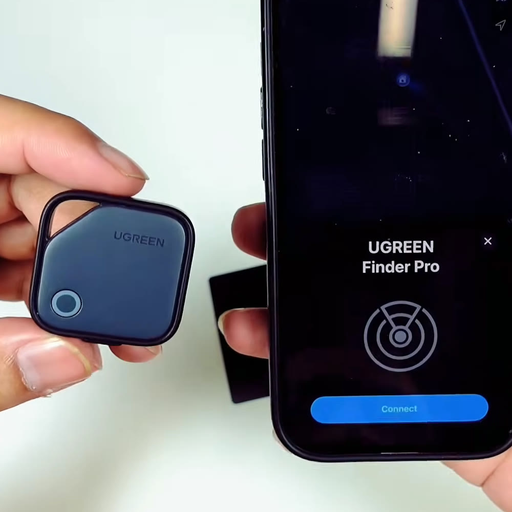 UGREEN FineTrack tracker tag held in hand showing its keyring loop and button, beside an iPhone displaying the UGREEN Finder Pro pairing screen